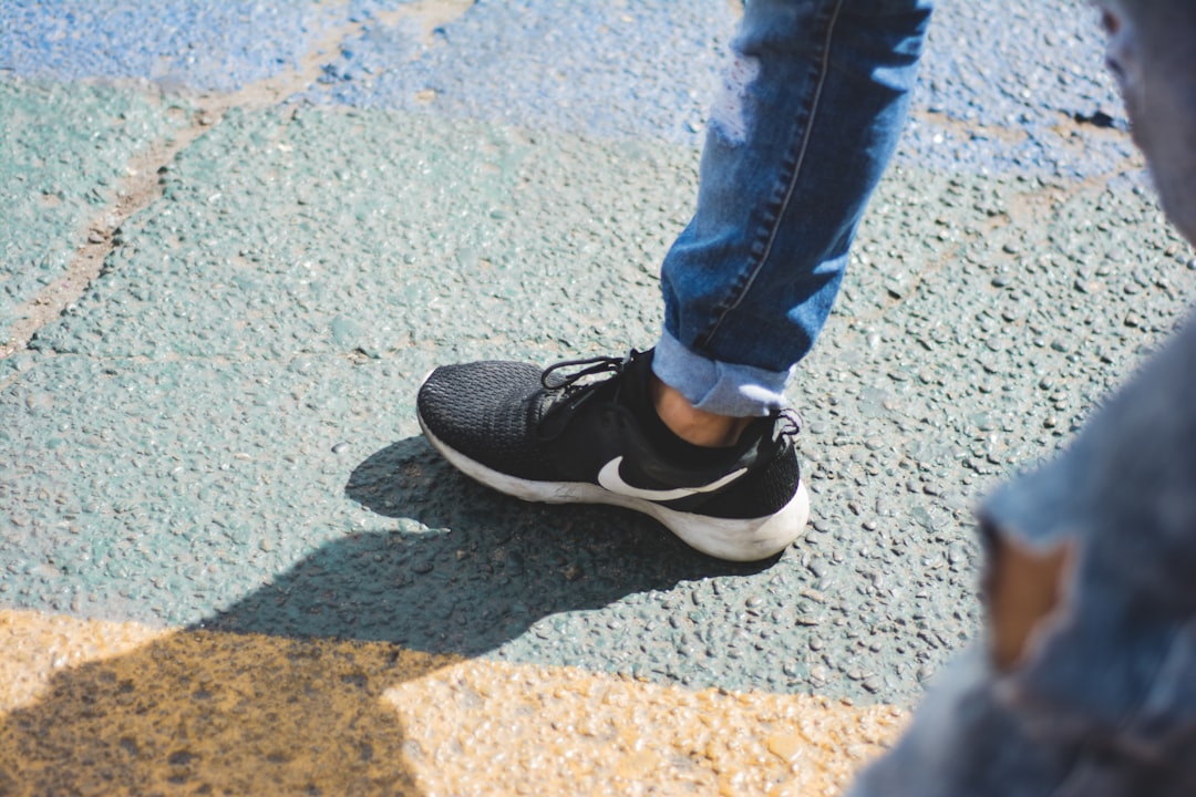 Close-up, moody shot of a runner sitting on a track, looking down thoughtfully at their old, worn-out running shoes.