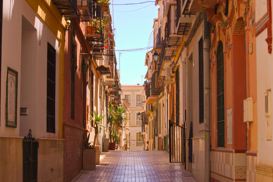 A quiet, sun-drenched street in a peaceful Los Cabos neighborhood with clean, white architecture and tropical plants, illustrating a tranquil living environment.